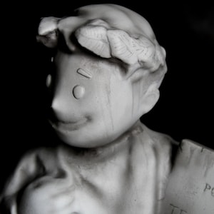 Può includere: Una statua in gesso bianco di una persona con una corona in testa. La statua tiene un cartello con la scritta "POST".