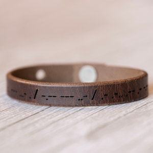 May include: A brown leather bracelet with a message in braille.