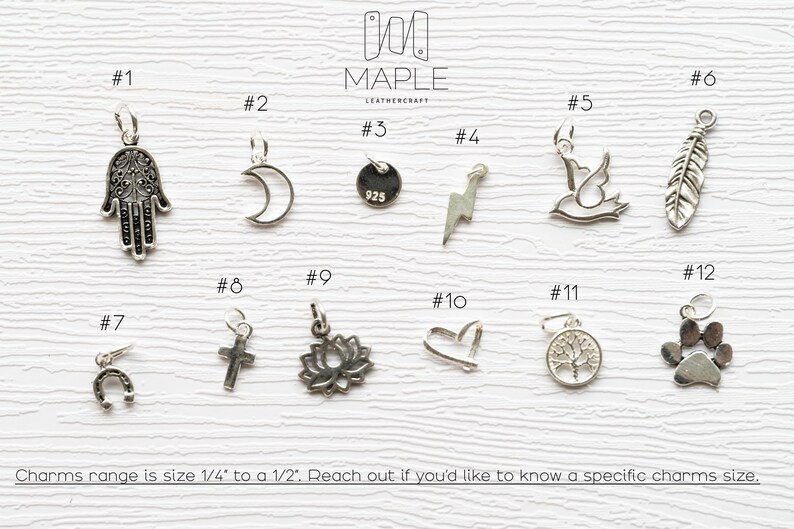 May include: A collection of twelve silver-toned metal charms labelled #1 through #12, including a hamsa, crescent moon, lightning bolt, bird, feather, horseshoe, cross, lotus, heart, tree, and paw print. Text states charms range from 0.6 cm to 1.3 cm.