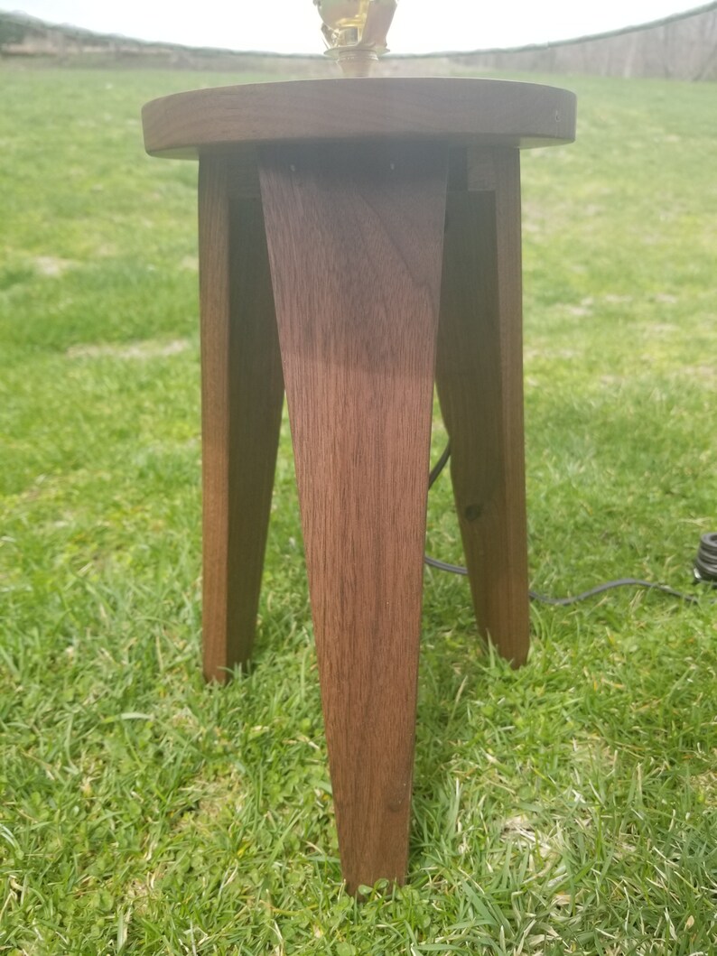 May include: A dark brown wooden table lamp base with a round top and three legs. The base is made of solid wood and has a natural finish.