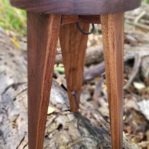 May include: A round wooden table with three legs. The table is made of dark wood and has a natural finish. The table is about 18 inches in diameter and 12 inches tall.