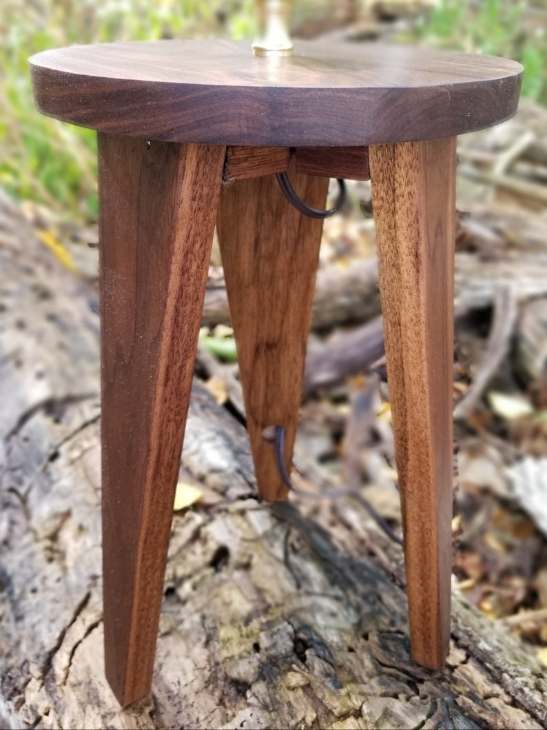 May include: A round wooden table with three legs. The table is made of dark wood and has a natural finish. The table is about 18 inches in diameter and 12 inches tall.