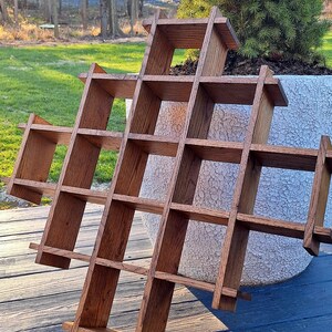 May include: A wooden wall shelf with a geometric design. The shelf is made of natural wood with a dark brown stain. It has multiple square compartments and is leaning against a white planter.