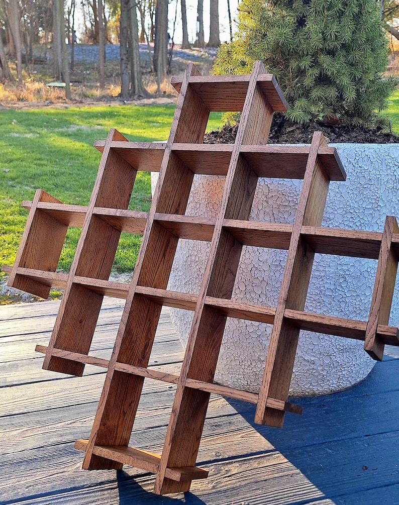 May include: A wooden wall shelf with a geometric design. The shelf is made of natural wood with a dark brown stain. It has multiple square compartments and is leaning against a white planter.