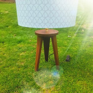 May include: A wooden tripod lamp base with a light blue lampshade featuring a geometric pattern. The lamp is on a grassy lawn.