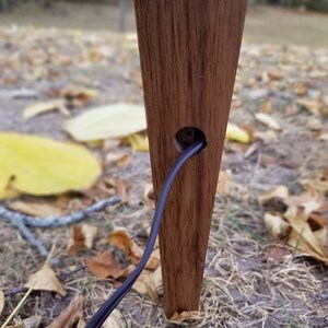 May include: A close-up of a wooden lamp base with a black electrical cord running through a hole in the base. The base is a dark brown color and has a natural wood grain.