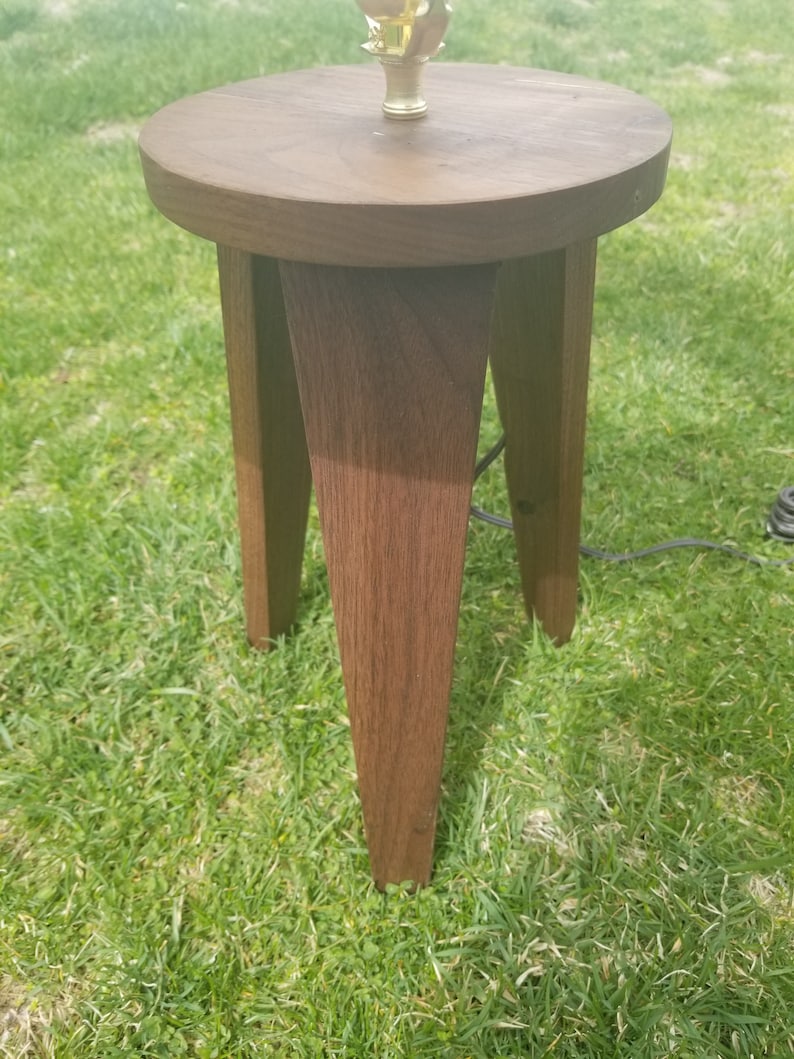 May include: A dark brown wooden lamp base with a round top and three legs. The base is made of solid wood and has a natural finish.