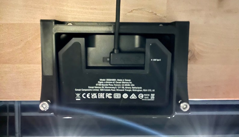 May include: Black rectangular device with a USB Type-C port and various certifications including CE, UKCA, EAC, FCC, and RoHS. The device is mounted on a wooden surface.