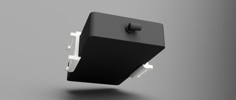 May include: A black rectangular box with white plastic clips on the sides. The box has a small black cap on the top.