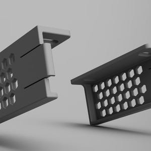 K&ouml;nnte beinhalten: Zwei graue, rechteckige Halterungen mit einem Wabenmuster aus sechseckigen Aussparungen. Die Halterungen haben eine rechtwinklige Form mit einer flachen Oberseite und einer Reihe kleiner L&ouml;cher. Das Design ist modern und minimalistisch.