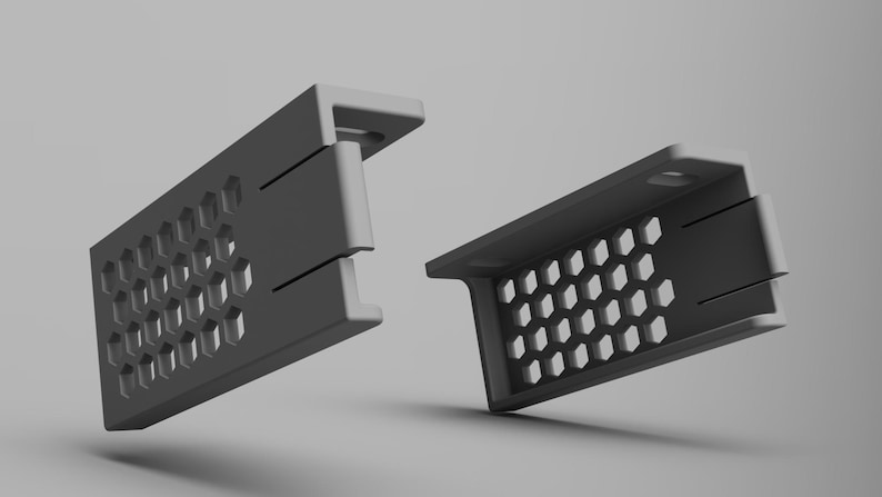 K&ouml;nnte beinhalten: Zwei graue, rechteckige Halterungen mit einem Wabenmuster aus sechseckigen Aussparungen. Die Halterungen haben eine rechtwinklige Form mit einer flachen Oberseite und einer Reihe kleiner L&ouml;cher. Das Design ist modern und minimalistisch.