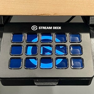 May include: A black Stream Deck with 15 customizable buttons. Each button has a blue, glowing light. The Stream Deck is mounted under a wooden surface.
