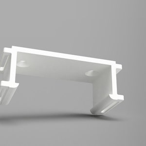 May include: White plastic bracket with two slots on each side and two holes on the top. The bracket is designed to hold a curtain rod.