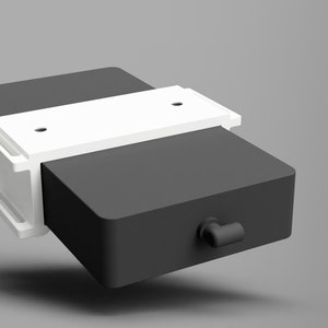 May include: A black rectangular box with a white plastic clamp on top. The box has a small black handle on the side.