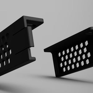 Puede incluir: Dos soportes negros rectangulares con un patrón de agujeros de panal. Los soportes tienen forma de ángulo recto con un labio en un lado. El fondo es un degradado de gris.