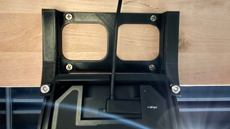 May include: A black 3D printed bracket with two rectangular cutouts, mounted to a wooden surface. A black cable is connected to a black device with the text "SOLID" and "1000 Type C" visible.