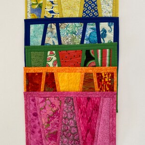Puede incluir: Una pila de cinco paneles de tela acolchada coloridos. Cada panel presenta un patrón diferente, incluyendo limones, coral, sandía y diseños abstractos. Los paneles están bordeados con colores coordinados.