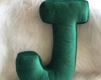 May include: A plush green letter J pillow. The pillow is made of a soft, velvety fabric and is perfect for adding a touch of personality to any room.