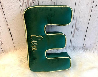 May include: A green velvet letter E pillow with gold trim and the name "Eva" embroidered on it.