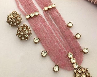 May include: A pink beaded necklace with a gold pendant and matching earrings. The pendant and earrings are adorned with clear stones.