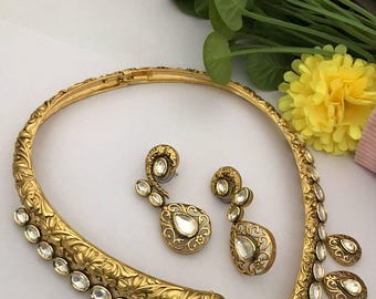 Può includere: Un girocollo dorato con un design floreale e pietre trasparenti. Il girocollo è abbinato a orecchini a goccia con pietre trasparenti.