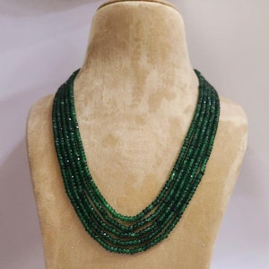 Può includere: Una collana multifilo realizzata con perline sfaccettate verde scuro. La collana è esposta su un busto di manichino marrone.