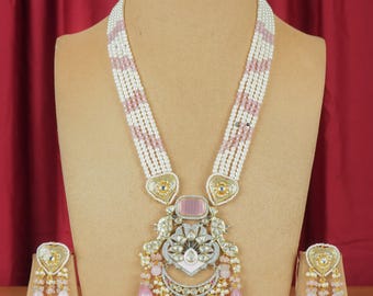 May include: A pink and white pearl necklace with a large, ornate pendant featuring pink and white stones. Matching pink and white pearl earrings with a heart-shaped design.
