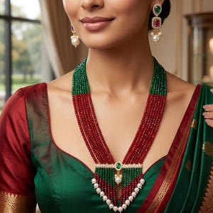 May include: A multi-strand necklace with green and red beads, accented with a pendant featuring a green stone and white pearls. Matching earrings with green and red stones and white pearls are also visible. The woman is wearing a green and red blouse.