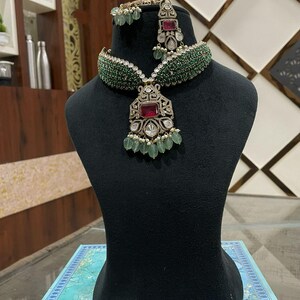 Könnte beinhalten: Ein grünes und silbernes Halskettenset mit einem großen roten Steinanhänger. Die Halskette hat einen Choker-Stil mit grünen Perlen und der Anhänger ist von kleineren Steinen umgeben.