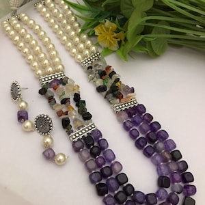 Puede incluir: Un collar de tres hilos con un hilo de perlas y dos hilos de piedras preciosas de color púrpura y multicolor. El collar tiene detalles plateados y viene con pendientes a juego.