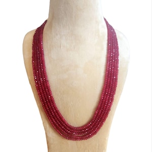 Può includere: Una collana multifilo realizzata con perline sfaccettate di colore rosso scuro. La collana è esposta su un busto di manichino in velluto beige.