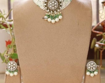 May include: An ornate necklace and earring set displayed on a mannequin. The choker-style necklace features a large, circular pendant with a floral design, accented with pearls and green beads. The earrings mirror the pendant's design.
