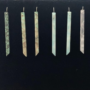 May include: Ten pairs of long, thin, rectangular earrings with a gold-coloured metal hook. The earrings are made of a light green, blue, or white material with a marbled or swirled pattern.