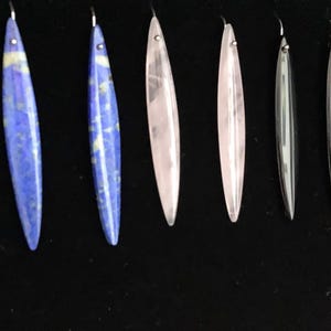 Puede incluir: Una colección de 10 pendientes largos y ovalados hechos de varios tipos de piedra. Los pendientes son todos de color plateado y tienen un diseño sencillo. Las piedras incluyen verde, azul, rosa, negro, blanco y marrón.