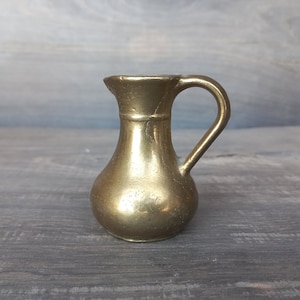 Op de afbeelding: Een kleine, gouden messing kan met een rond lichaam en een handvat. De kan heeft een gladde, gepolijste afwerking.