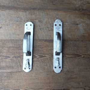 May include: Two silver door handles with a simple design. The handles are rectangular in shape with a rounded top and bottom. The handles are mounted on a wooden surface.