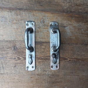 May include: Two silver door handles with a rounded design and a small decorative knob. The handles are mounted on a wooden surface.