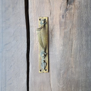 May include: A brass door handle with a decorative design. The handle is mounted on a wooden door.
