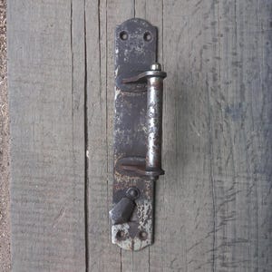 May include: A rusty metal door handle with a silver metal lever. The handle is attached to a wooden door.