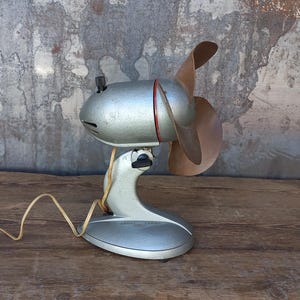 May include: A vintage silver and brown desk fan with a red accent on a wooden surface.