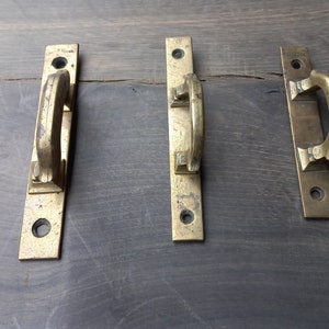 May include: Three antique brass door handles with a simple design. The handles are rectangular with a rounded top and bottom. Each handle has a single loop for pulling the door open.