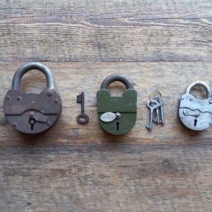 May include: Three vintage padlocks with keys on a wooden surface. The padlocks are of different sizes and have a rustic, aged look. The keys are silver and have a simple design.