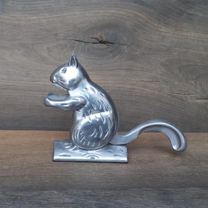 May include: A silver squirrel nutcracker with a long tail that acts as a lever. The squirrel is sitting on a base with a textured surface.