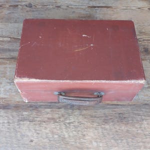 May include: A vintage red suitcase with a brown leather handle.