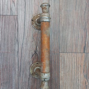 May include: A vintage door pull with a wooden handle and ornate metal accents. The handle is a warm brown color, and the metal components have a tarnished, antique finish. The door pull is mounted on a wooden surface.