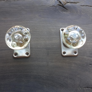 Puede incluir: Dos pomos de puerta de vidrio transparente con superficie texturizada, montados en placas rectangulares plateadas.