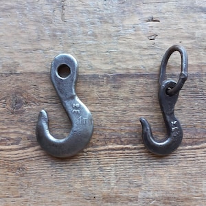 Puede incluir: Dos ganchos de metal, uno con un anillo. Ambos ganchos son de color plateado y tienen marcas. El gancho de la izquierda tiene las marcas "2 T 1" y "20", mientras que el gancho de la derecha tiene las marcas "1 T" y "20".