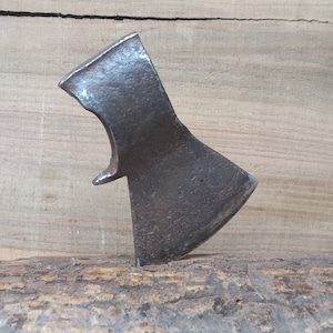 May include: A rusty, metal axe head with a slightly curved blade. The axe head is resting on a piece of wood.