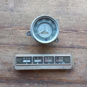 Könnte beinhalten: Ein Vintage-Armaturenbrett mit einem runden Tachometer, der bis zu 140 km/h anzeigt, und einem rechteckigen Panel mit fünf Anzeigen: einer Batterieanzeige, einer Tankanzeige, einer Temperaturanzeige, einer Druckanzeige und einer Warnleuchte.