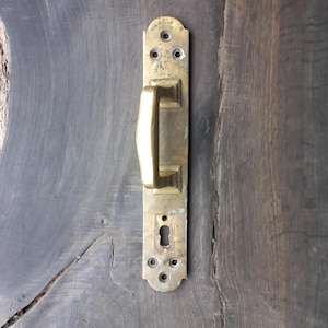 May include: A brass door handle with a keyhole and a rectangular shape. The handle is mounted on a wooden door.